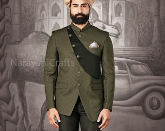 Puede incluir: Un traje verde oliva con cuello mandarín, faja negra y pantalón a juego. La persona lleva un turbante dorado y zapatos marrones. El fondo presenta un mural detallado con elementos arquitectónicos y un coche antiguo.