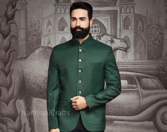 Puede incluir: Chaqueta Nehru verde oscuro con cuello mandarín y botones dorados, combinada con pantalones de vestir negros. La chaqueta tiene un corte entallado. El fondo presenta un mural con imágenes arquitectónicas y animales.