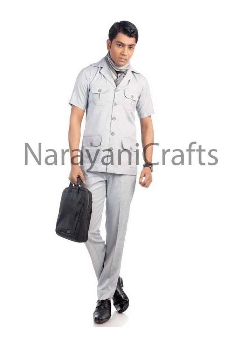 May include: A man wearing a light gray short-sleeved collared shirt with a light gray scarf and matching pants. He is holding a black briefcase and is standing on a white background.