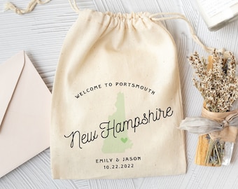 May include: A white drawstring bag with the text "Welcome to Portsmouth New Hampshire" and a green outline of the state of New Hampshire. The bag also includes the text "Emily & Jason 10.22.2022".
