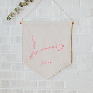 May include: A white canvas banner with a pink outline of the Pisces constellation and the word "Pisces" written in pink script.