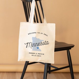 May include: A white tote bag with a blue outline of the state of Minnesota and the text "Welcome to St. Paul, Minnesota" and "Aaron & Maycie 05.22.2023".