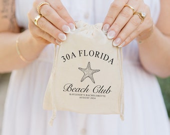 May include: A white drawstring bag with the text "30A Florida Beach Club" and a starfish graphic. The text below the graphic reads "Kayleigh's Bachelorette August 2024".
