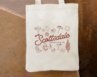 Könnte beinhalten: Eine weiße Canvas-Tragetasche mit rotem Text und Illustrationen. Der Text lautet "Scottsdale Makenna's Bach 2024" und die Illustrationen zeigen Kakteen, Sonnenbrillen, ein Margarita-Glas, einen Cowboystiefel und einen Bikini. Die Tasche hat einen roten Riemen mit dem Namen "Maddie" darauf gedruckt.