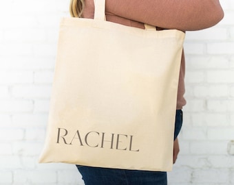 Puede incluir: Una bolsa de lona beige con el nombre "RACHEL" impreso en marrón en la parte delantera.