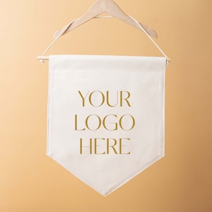 May include: A cream-coloured banner with the text "YOUR LOGO HERE" in gold lettering. The banner is hanging from a wooden hanger and a wooden rod. The background is a solid, light orange colour.