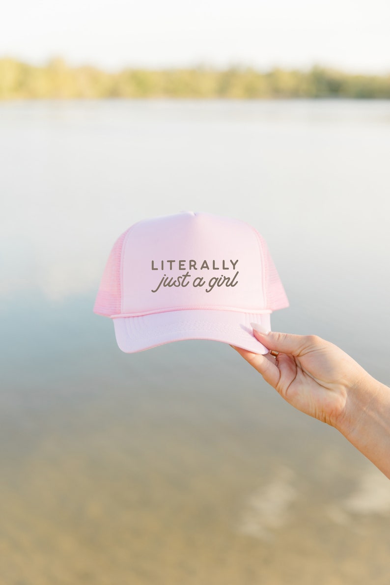 May include: Pink trucker hat with a brown embroidered design that says "LITERALLY just a girl".