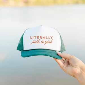 May include: A green and white trucker hat with the text "LITERALLY just a girl" in orange.