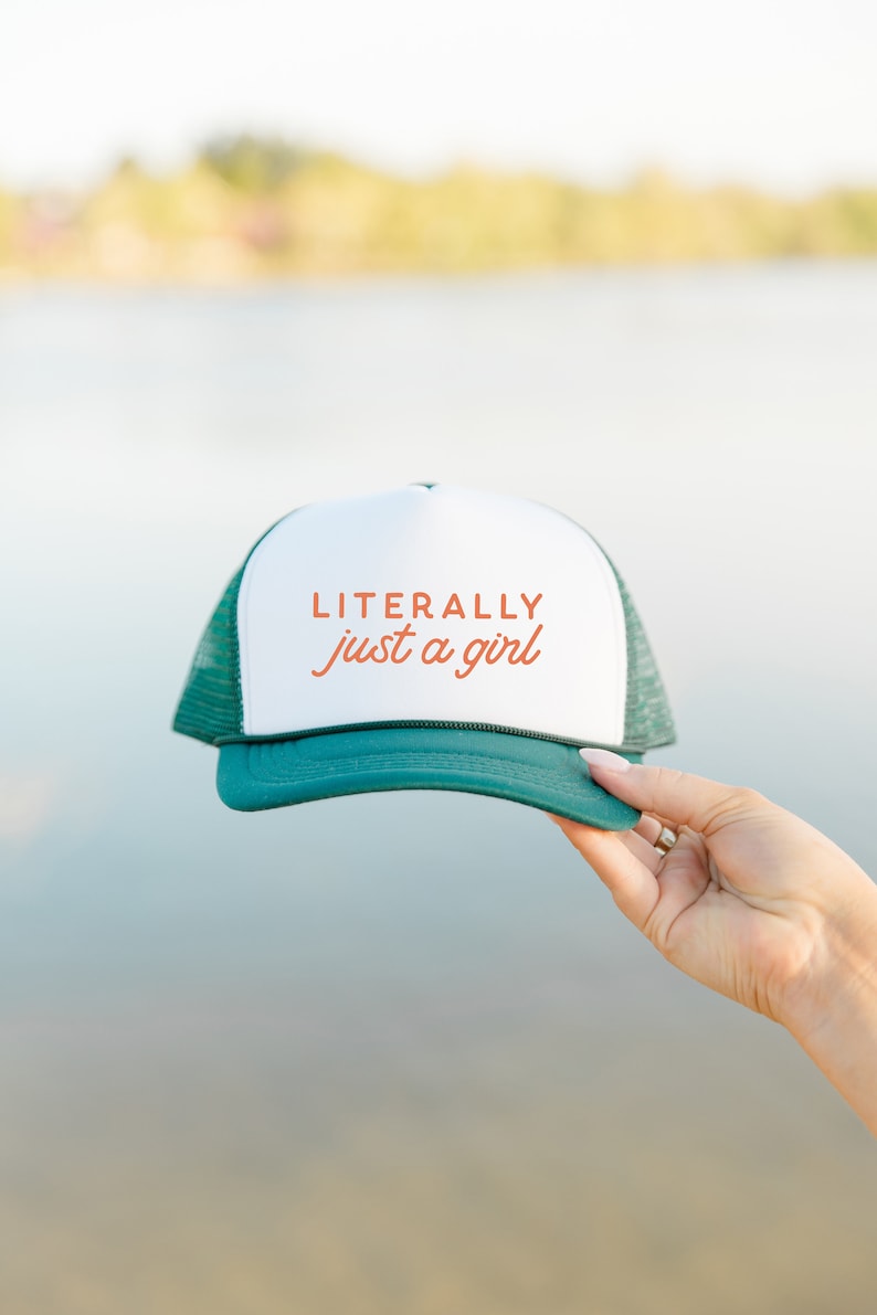 May include: A green and white trucker hat with the text "LITERALLY just a girl" in orange.