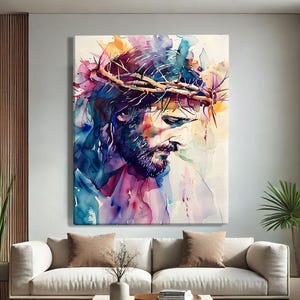 Può includere: Un quadro rettangolare su tela raffigurante un ritratto ad acquerello di una figura barbuta che indossa una corona di spine. L'opera utilizza vivaci schizzi di toni blu, viola, rosa e arancioni su uno sfondo chiaro e neutro.