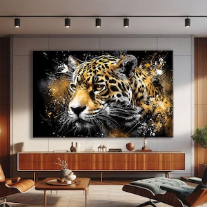 May include: A large canvas print of a jaguar's face, rendered in a striking artistic style. The image uses black, gold, and white paint splashes to create a dynamic effect. The jaguar's fur is detailed with spots, and its eyes are a warm amber. The artwork is displayed in a contemporary living room.