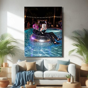 Peut inclure: Impression sur toile d'une personne en casque rose et costume à paillettes, lisant dans un flotteur de piscine boule à facettes. La piscine est entourée de palmiers et d'une fête nocturne. L'œuvre est affichée au-dessus d'un canapé bleu clair.