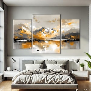 Puede incluir: Una obra de arte en lienzo de tres paneles que representa un paisaje montañoso en tonos grises, blancos y naranjas. La pintura abstracta presenta pinceladas y un elemento de agua reflectante. La obra de arte se exhibe sobre una cama en un dormitorio moderno.