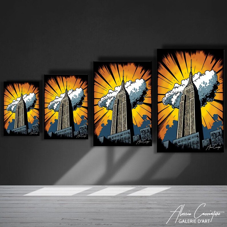 May include: Four framed art prints of the Empire State Building in a pop art style. The artwork features the iconic skyscraper against a yellow and orange burst background with stylized clouds and a blue sky. The prints are displayed on a dark gray wall.