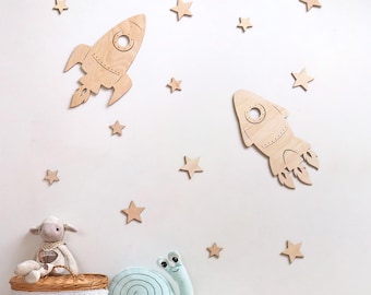 May include: Two wooden rocket ship wall decorations with a light brown finish. The rockets are surrounded by small wooden stars in a light brown finish.