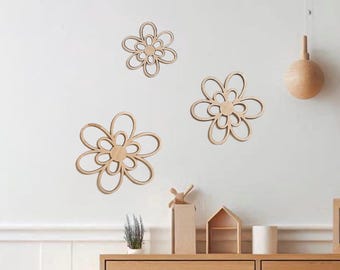 Könnte beinhalten: Drei Wanddekorationen aus Holz in Form von Blumen mit natürlicher Holzoberfläche. Jede Blume hat eine kreisförmige Mitte und geschwungene Blütenblätter. Die Blumen sind an einer weißen Wand befestigt.