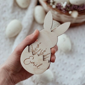 May include: A wooden Easter bunny ornament with a cracked egg design. The egg is decorated with a floral pattern and the name "Emil" is engraved inside.