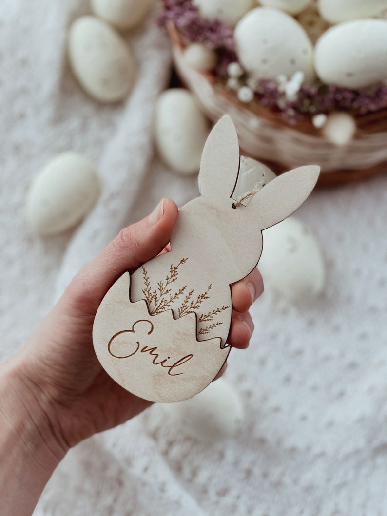 May include: A wooden Easter bunny ornament with a cracked egg design. The egg is decorated with a floral pattern and the name "Emil" is engraved inside.