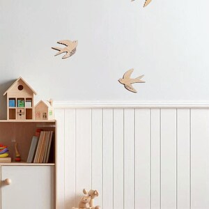 Puede incluir: Decoraci&oacute;n de pared de madera con forma de golondrinas de varios tama&ntilde;os, montada en una pared blanca. La habitaci&oacute;n tambi&eacute;n cuenta con una estanter&iacute;a de madera con juguetes y libros, y un tren de juguete de madera. El tema general es una habitaci&oacute;n infantil.