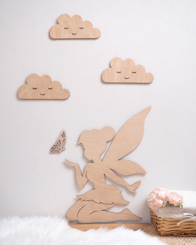 May include: Wooden fairy silhouette with wings, holding a butterfly, with three wooden clouds with smiling faces on a white wall.