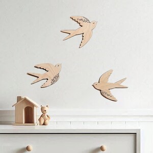 There are three wooden swallows on the wall. Swallows have floral engraving.