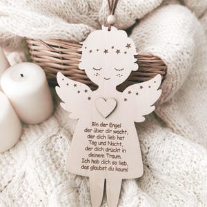 Puede incluir: Adorno de &aacute;ngel de madera con detalles de coraz&oacute;n y estrellas, con un lazo de cuero marr&oacute;n para colgar. El &aacute;ngel tiene una cara dulce y alas. Texto en alem&aacute;n grabado en el cuerpo del &aacute;ngel.