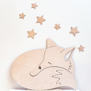 May include: A wooden cutout of a sleeping fox with a curled tail. The fox is surrounded by small wooden stars.