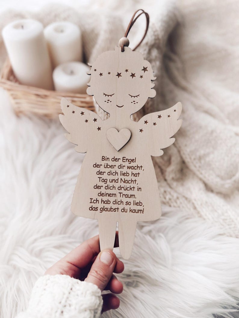 Puede incluir: Adorno de &aacute;ngel de madera con detalles de coraz&oacute;n y estrellas. El &aacute;ngel tiene los ojos cerrados y alas. El texto en el &aacute;ngel dice: "Bin der Engel der &uuml;ber dir wacht, der dich lieb hat Tag und Nacht, der dich dr&uuml;ckt in deinem Traum. Ich hab dich so lieb, das glaubst du kaum!"