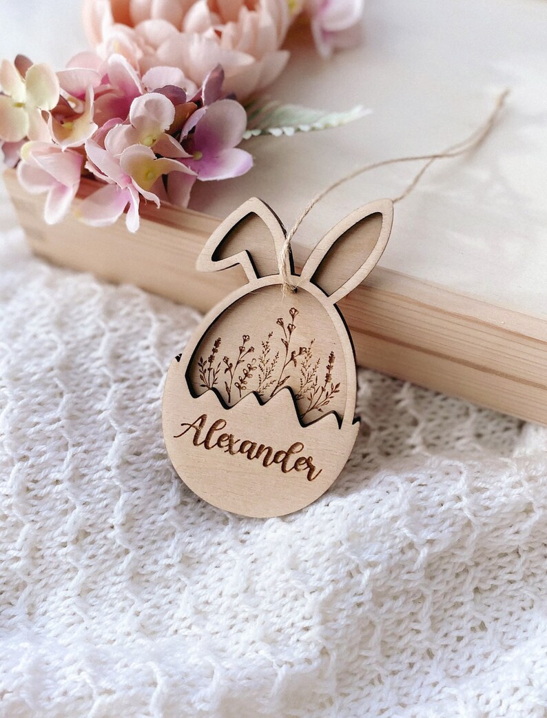 May include: A wooden Easter egg ornament with bunny ears, featuring a floral design and the name "Alexander" engraved on the front.