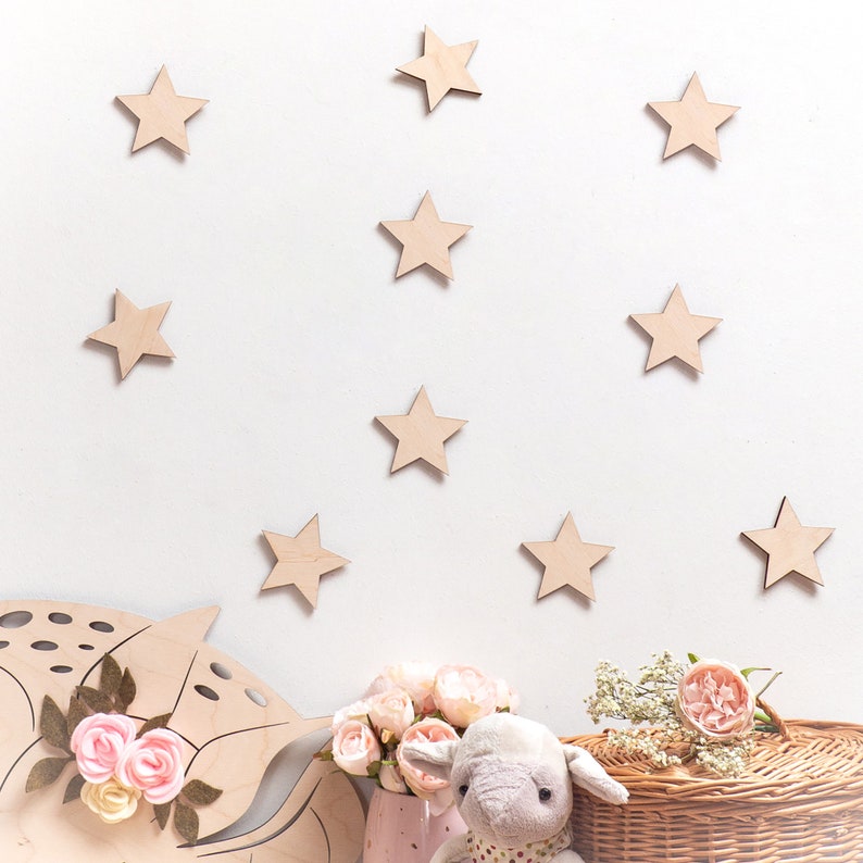 Peut inclure: Un mur blanc d&eacute;cor&eacute; d'&eacute;toiles en bois, avec un &eacute;l&eacute;phant en peluche assis sur un panier en osier. Il y a des fleurs roses dans un vase rose.