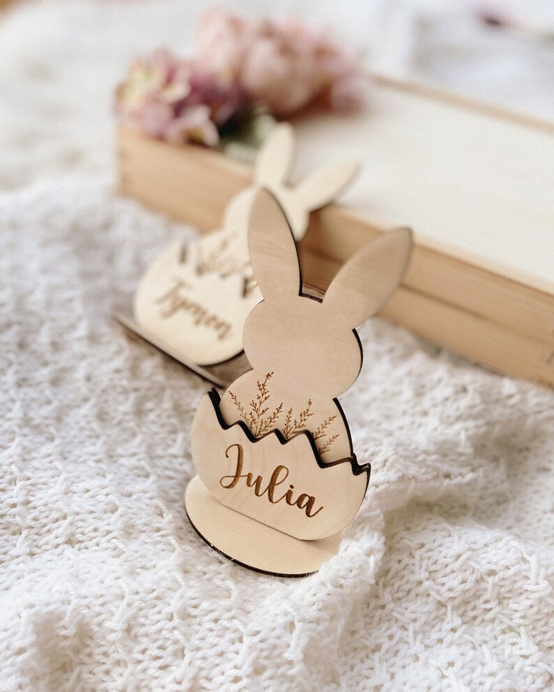 May include: Wooden Easter bunny place card with a name tag that says "Julia". The bunny is holding an egg with a floral design.
