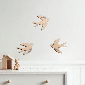 There are three wooden swallows on the wall. Swallows have floral engraving.