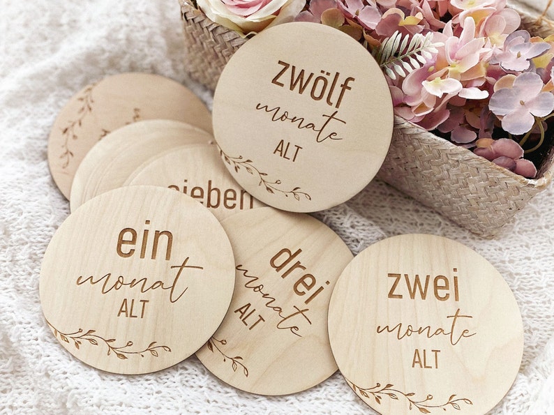 May include: Wooden baby milestone discs with German text, including "ein monat alt", "zwei monate alt", "drei monate alt", and "zwolf monate alt".