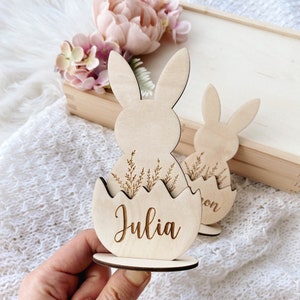 May include: Wooden Easter bunny place card with a name, "Julia", engraved on the egg. The bunny is holding a nest of grass.