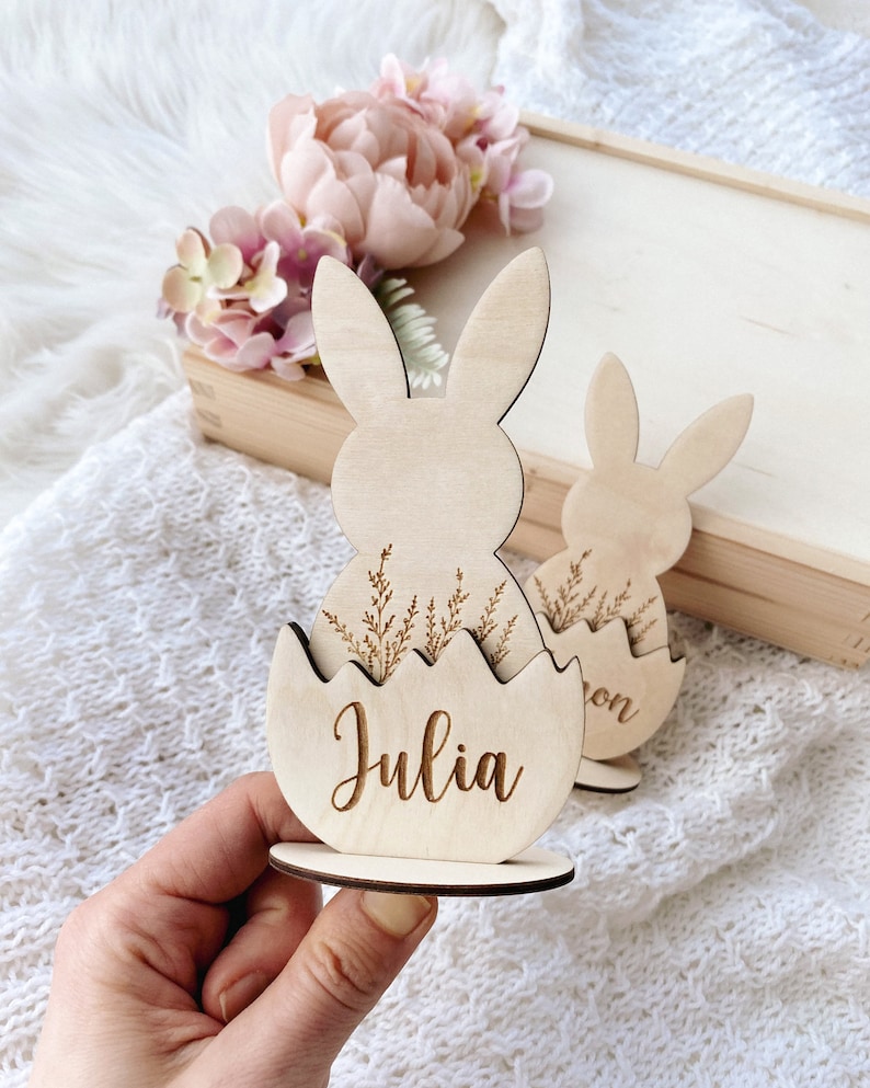 May include: Wooden Easter bunny place card with a name, "Julia", engraved on the egg. The bunny is holding a nest of grass.