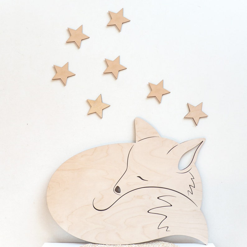 Peut inclure: Une d&eacute;coupe en bois d'un renard endormi avec une queue enroul&eacute;e, entour&eacute;e de sept petites &eacute;toiles en bois. Le renard et les &eacute;toiles sont de couleur brun clair.