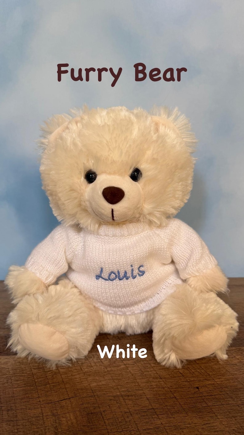 May include: A plush, cream-colored teddy bear with the text "Furry Bear" above it. The bear wears a white sweater with the name "Louis" embroidered in blue. The word "White" is below the bear.