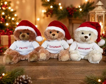 May include: Three plush teddy bears sitting in a row, each wearing a red Santa hat and a white knitted sweater. The sweaters feature red embroidered text reading Merry, Christmas, and Everyone! from left to right. The bears have soft fur.