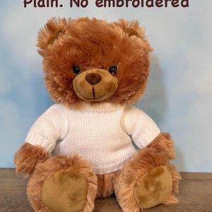 May include: A brown teddy bear wearing a white sweater. The bear has a soft, plush fur and a friendly expression. The text "Plain. No embroidered" is visible in the image.