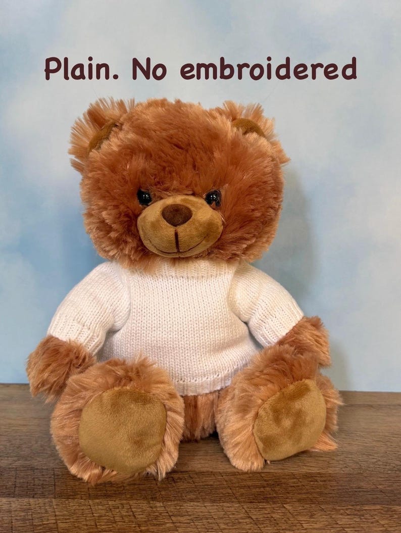 May include: A brown teddy bear wearing a white sweater. The bear has a soft, plush fur and a friendly expression. The text "Plain. No embroidered" is visible in the image.