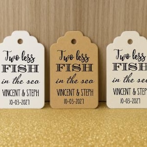 Può includere: Tre etichette regalo decorative, color crema e marrone, con bordi smerlati. Presentano la scritta "Two less FISH in the sea", i nomi "VINCENT & STEPH" e la data "10-03-2027".