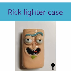 Peut inclure: Un étui à briquet rectangulaire présentant un visage sculpté couleur chair avec de grands yeux blancs, des pupilles noires, un sourcil bleu et une bouche ouverte montrant des dents et une petite goutte verte. Le texte "Rick lighter case" est visible.