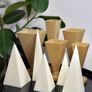 May include: A set of six white pyramid candles and six brown geometric candle holders. The candles are arranged on a black surface.