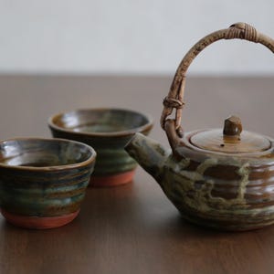 Può includere: Servizio da tè in ceramica con teiera con manico intrecciato e due tazze abbinate. Il set ha una glassa marrone e verde con base rossa, perfetto per servire il tè.