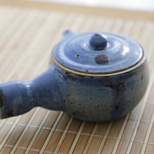 Könnte beinhalten: Eine blaue Teekanne aus Keramik mit Deckel und Ausguss. Die Teekanne hat eine gesprenkelte Glasur und einen rustikalen Look.