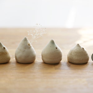 May include: Five small, ceramic, cone-shaped incense holders in various shades of white and beige. The holders are arranged in a row on a wooden surface. A single silver coin is to the right of the holders.