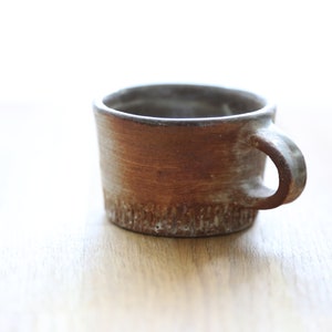 Op de afbeelding: Een kleine, bruine keramische mok met een getextureerd oppervlak en een eenvoudige handgreep.
