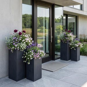 May include: Three dark grey rectangular planters filled with colourful flowers in front of a modern home's entrance. The flowers include purple, white, and lavender blooms. The planters are different heights.