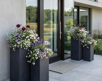 May include: Three dark gray rectangular planters filled with colorful flowers in front of a modern home's entrance. The flowers include purple, white, and lavender blooms. The planters are different heights.