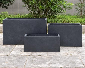 Puede incluir: Un conjunto de tres maceteros rectangulares con un acabado en gris carbón oscuro. Los maceteros están dispuestos en una formación escalonada, con paredes sólidas y lisas y aberturas superiores.
